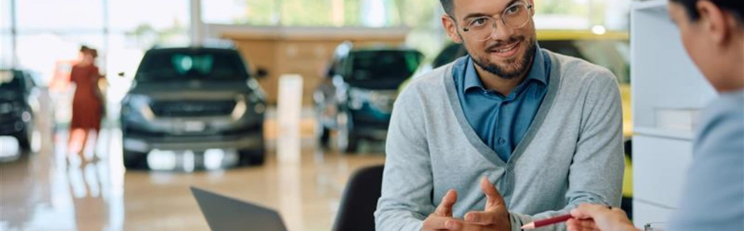 men sitting at desk in car dealership with cars in the background